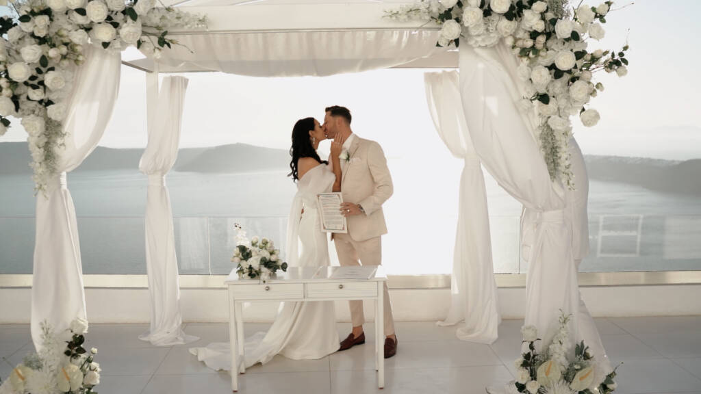 Bianca and Joseph beneath the white floral ceremony canopy at Andromeda Santorini