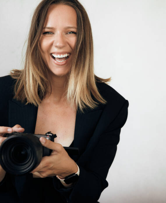 Daria Meshkova, founder of Santorini.video and wedding videographer, smiling while holding a camera.