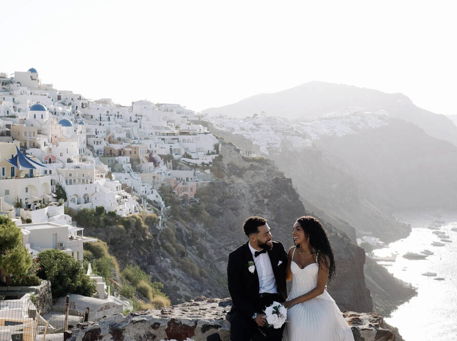 Beeminet looking at Donovan during their sunrise vow exchange, with Oia’s whitewashed buildings behind her.